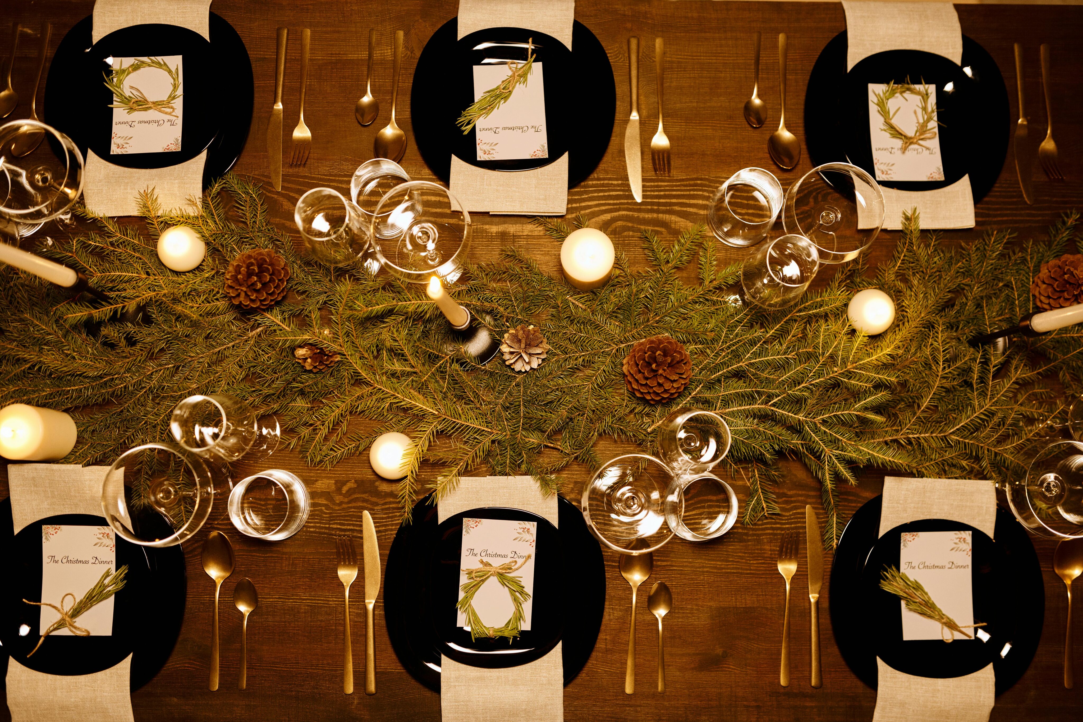 A festive New Year's Eve dining table is set with candles, pine branches, glassware, and plates, each with a menu for the special dinner.